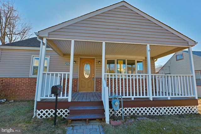 view of front facade with brick siding, a porch, and roof with shingles