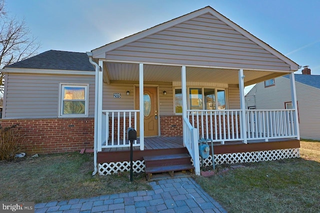 bungalow-style house featuring brick siding, covered porch, and a shingled roof