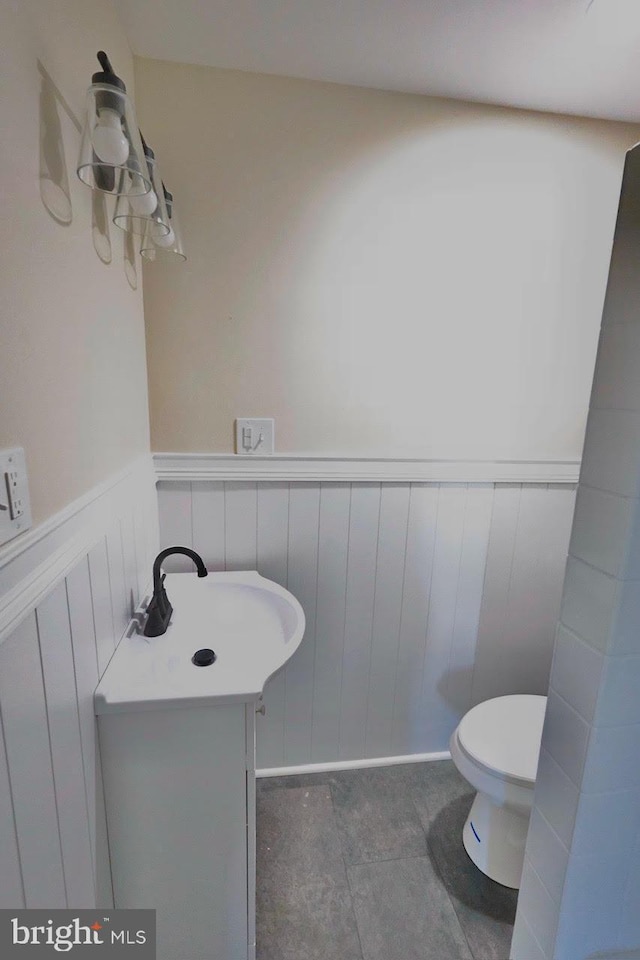 half bath featuring a wainscoted wall, toilet, and a sink