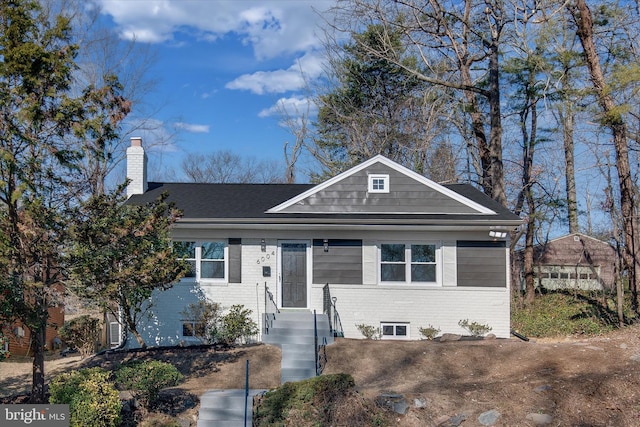 view of front of house featuring a shingled roof, brick siding, and a chimney