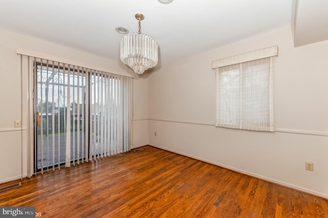 spare room featuring visible vents, an inviting chandelier, and wood finished floors