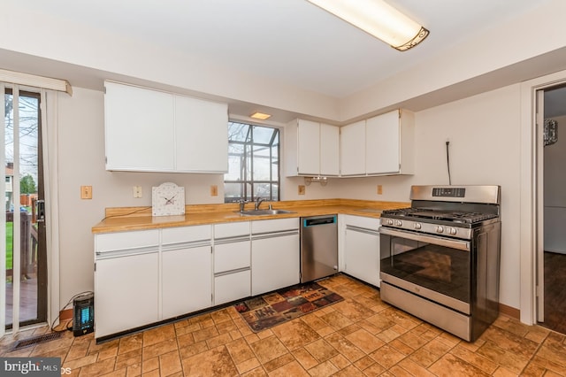 kitchen with white cabinets, appliances with stainless steel finishes, stone finish flooring, and a sink