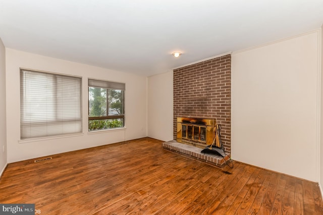 unfurnished living room with visible vents, wood-type flooring, and a brick fireplace