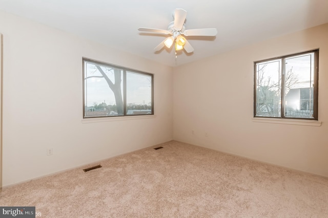 empty room featuring visible vents, carpet floors, and ceiling fan