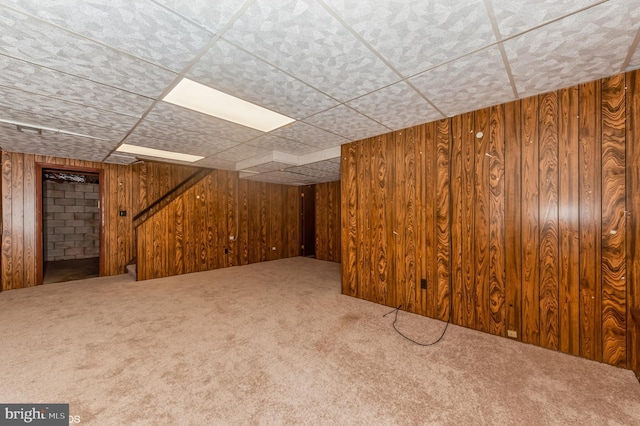 finished basement with a drop ceiling, carpet, and wood walls