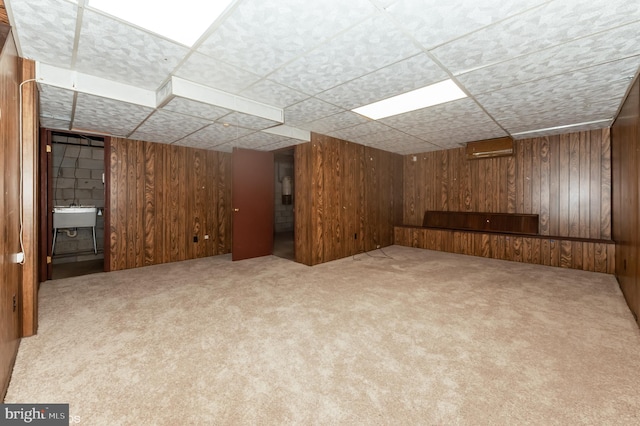 finished below grade area with wooden walls, carpet flooring, a paneled ceiling, and a sink