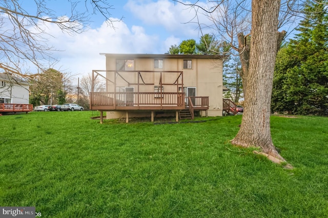 rear view of property with a deck, a yard, and stucco siding