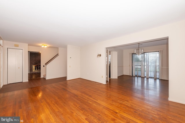 unfurnished living room featuring a brick fireplace, a notable chandelier, and wood finished floors