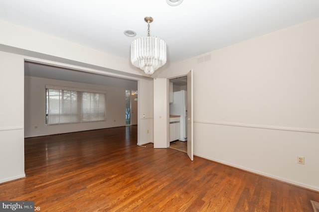 spare room with visible vents, baseboards, an inviting chandelier, and wood finished floors