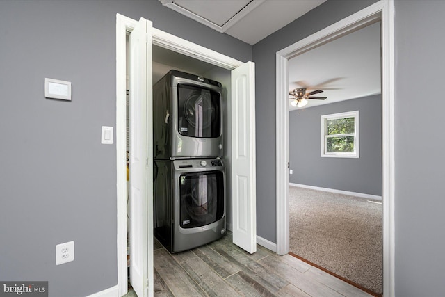 clothes washing area featuring baseboards, stacked washer and dryer, laundry area, wood finished floors, and a ceiling fan