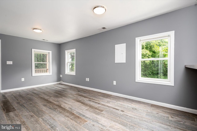 empty room featuring wood finished floors, visible vents, a wealth of natural light, and baseboards