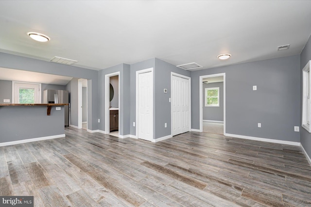 unfurnished living room featuring visible vents, baseboards, and wood finished floors