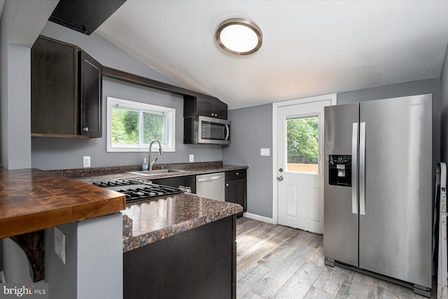 kitchen featuring light wood-style flooring, a sink, appliances with stainless steel finishes, baseboards, and vaulted ceiling