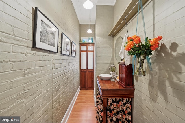 corridor featuring light wood-style flooring, brick wall, and a sink