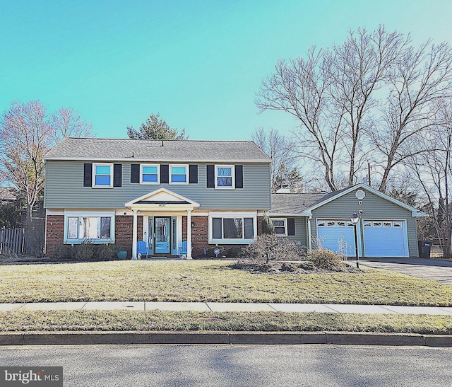 colonial house featuring aphalt driveway, an attached garage, brick siding, and a front lawn