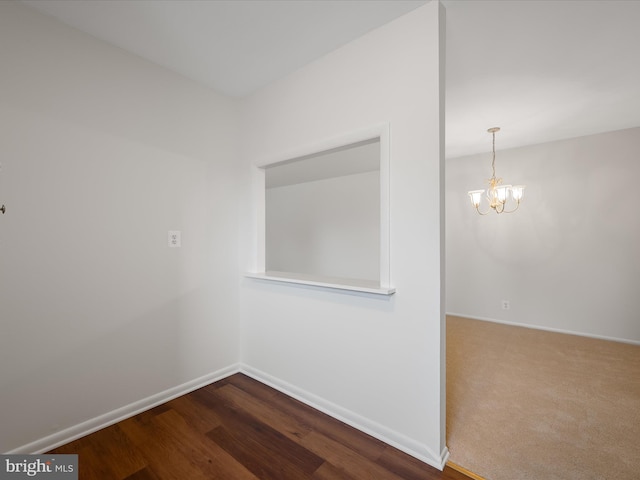 spare room featuring baseboards, a notable chandelier, and dark wood finished floors