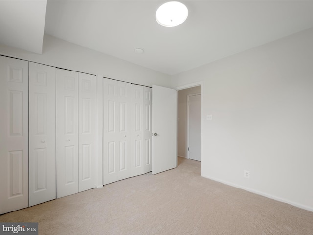 unfurnished bedroom featuring baseboards, multiple closets, and light carpet