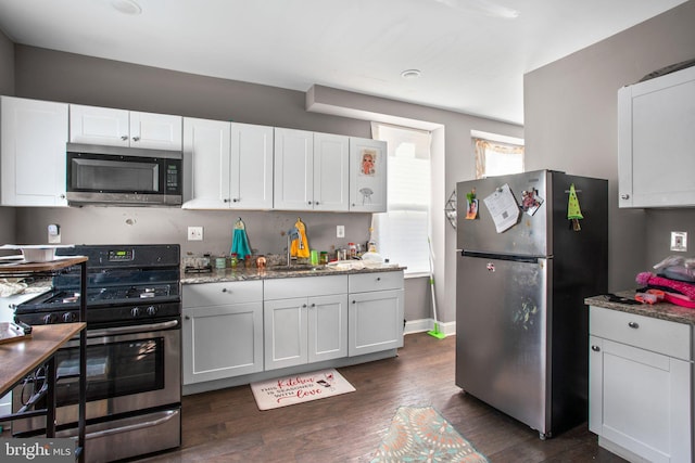 kitchen with light stone countertops, dark wood-style flooring, a sink, stainless steel appliances, and white cabinets