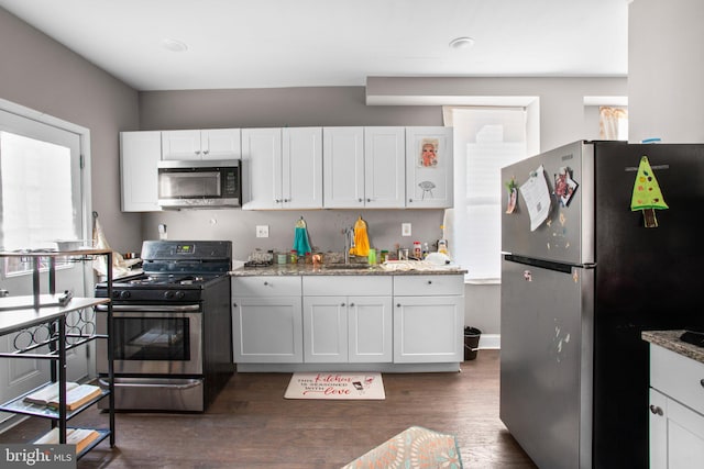 kitchen featuring light stone countertops, stainless steel appliances, dark wood-style floors, white cabinetry, and a sink