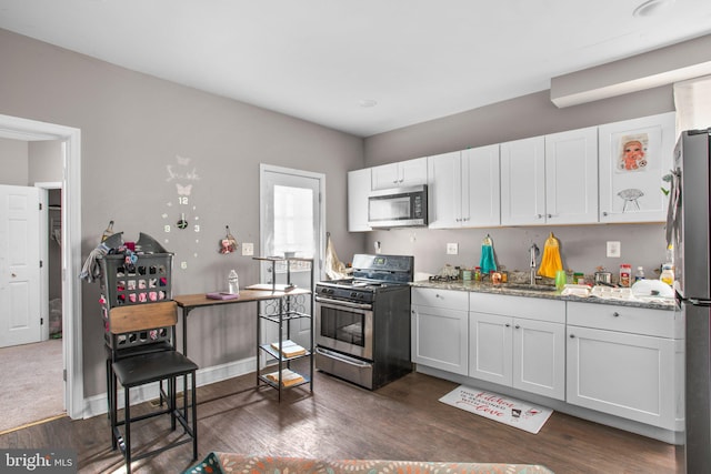 kitchen with light stone counters, dark wood-style floors, a sink, white cabinets, and appliances with stainless steel finishes