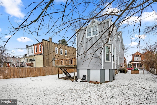 snow covered property with a wooden deck, a residential view, stairway, and fence