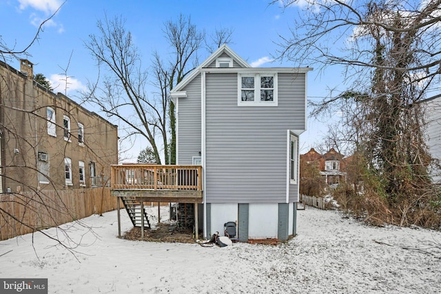 snow covered back of property with a wooden deck and stairs