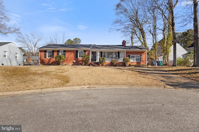 ranch-style house featuring brick siding, covered porch, a chimney, and a front lawn