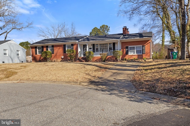 single story home with brick siding, covered porch, and a chimney