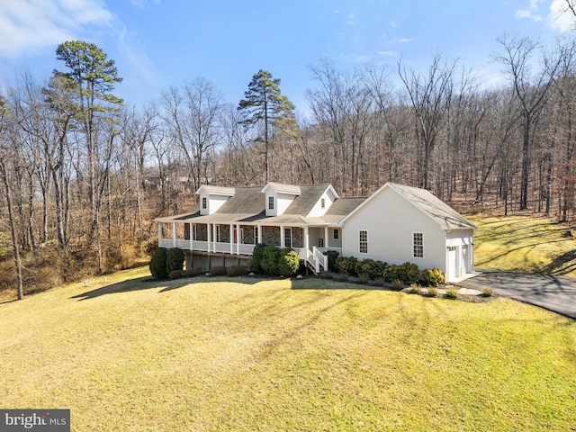 cape cod home with a front yard, covered porch, a garage, aphalt driveway, and a view of trees