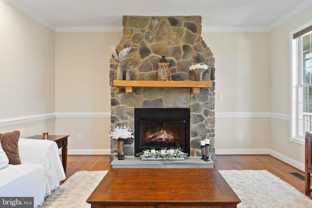 living area with a stone fireplace, a healthy amount of sunlight, ornamental molding, and wood finished floors