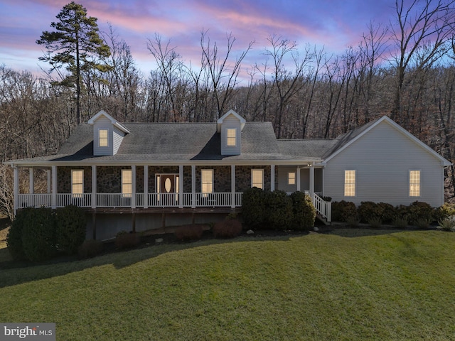 view of front facade featuring stone siding, a lawn, a porch, and roof with shingles