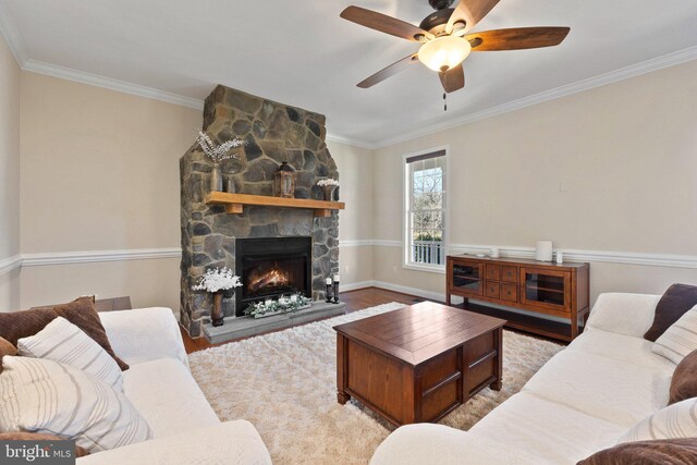 living room featuring a stone fireplace, crown molding, ceiling fan, and wood finished floors