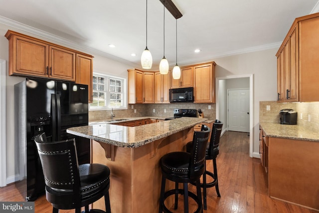 kitchen featuring dark wood-type flooring, black appliances, ornamental molding, a sink, and a center island