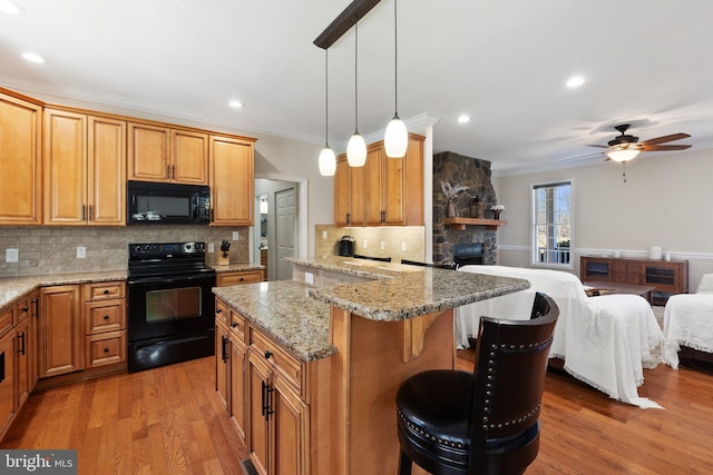 kitchen with light wood-type flooring, ornamental molding, black appliances, a kitchen breakfast bar, and open floor plan