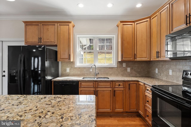 kitchen featuring black appliances, a sink, wood finished floors, crown molding, and light stone countertops