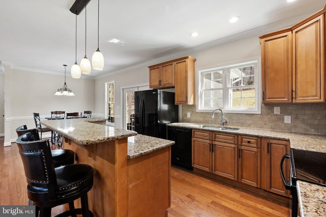 kitchen featuring a breakfast bar, light wood-style flooring, a sink, black appliances, and backsplash