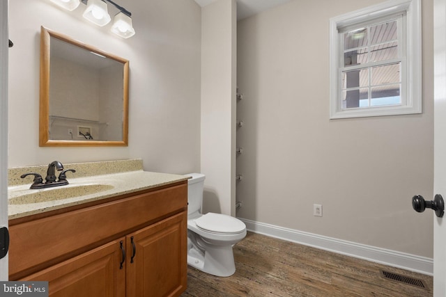 half bathroom featuring visible vents, toilet, wood finished floors, baseboards, and vanity