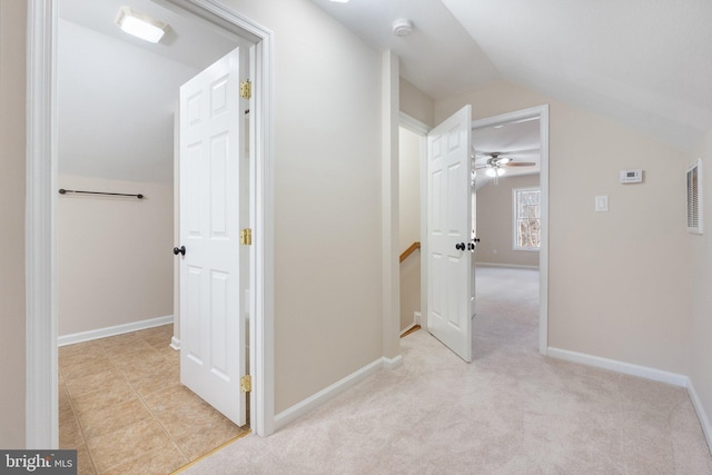 hallway featuring lofted ceiling, baseboards, and light carpet