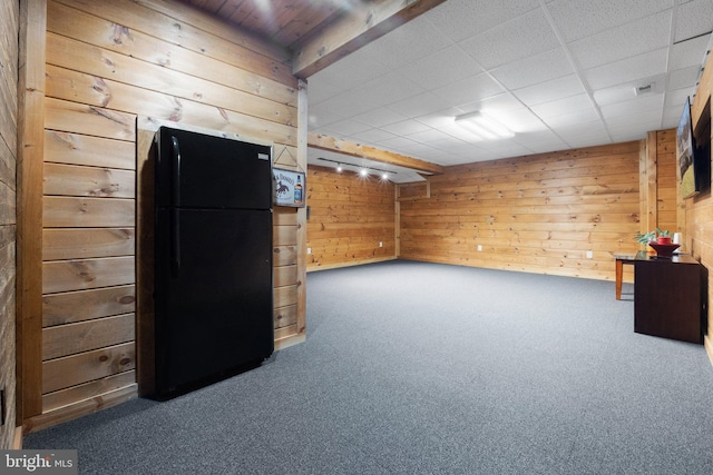 finished below grade area featuring a drop ceiling, carpet floors, wooden walls, and freestanding refrigerator