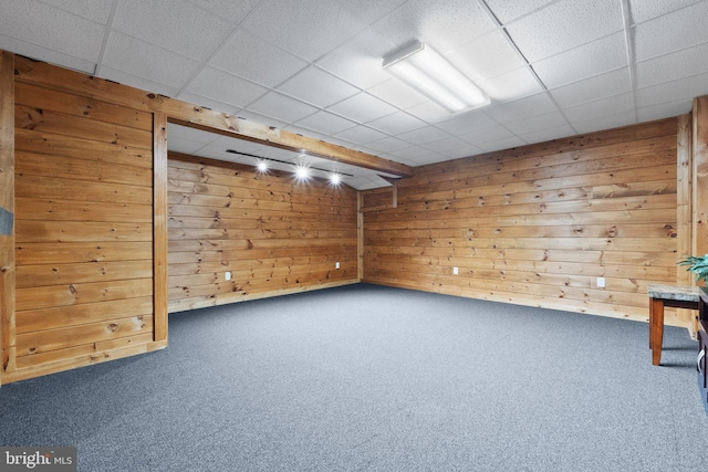 unfurnished room with a drop ceiling, carpet floors, and wooden walls