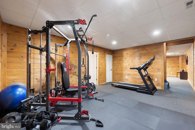 exercise room with a drop ceiling, visible vents, and wooden walls