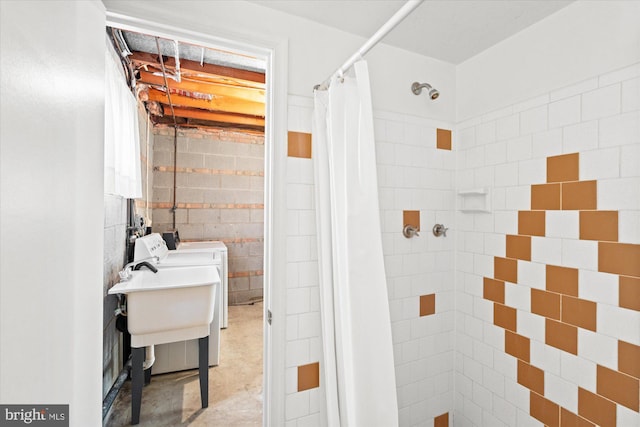 full bathroom with concrete block wall, independent washer and dryer, and a tile shower