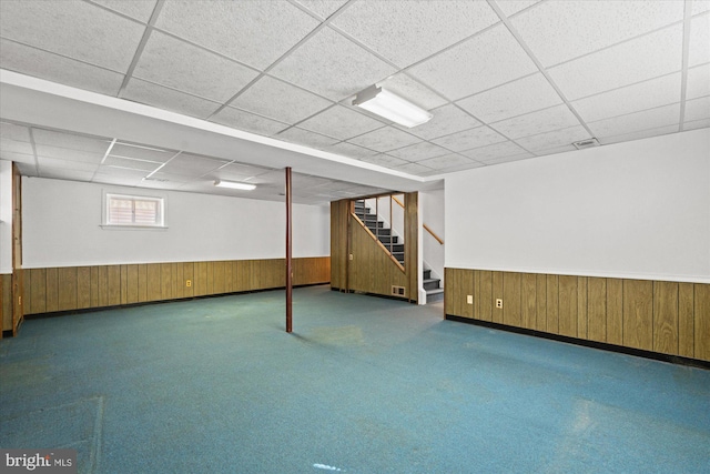 below grade area featuring a wainscoted wall, wood walls, and stairs