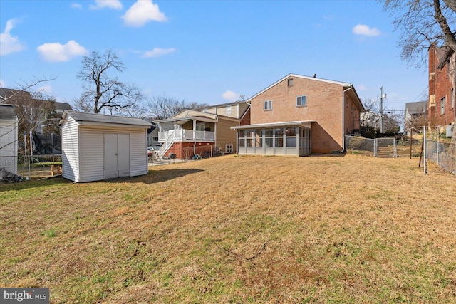 rear view of property featuring a storage unit, an outbuilding, a lawn, a fenced backyard, and a sunroom