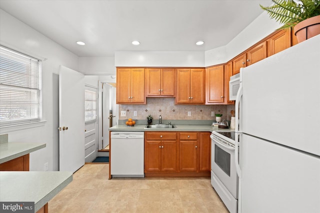 kitchen with a sink, white appliances, backsplash, and light countertops