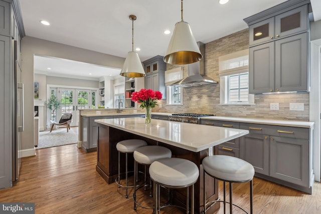 kitchen featuring range hood, a peninsula, wood finished floors, decorative backsplash, and a kitchen island