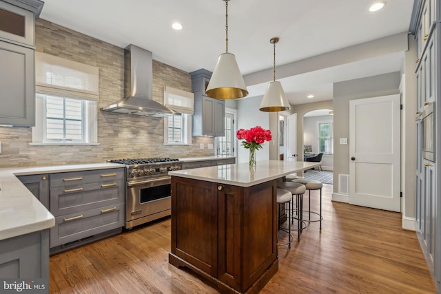 kitchen featuring premium stove, wall chimney exhaust hood, gray cabinetry, arched walkways, and light countertops