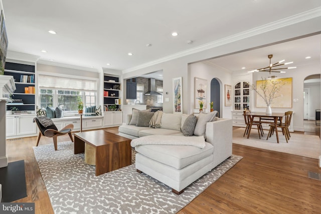 living area featuring arched walkways, wood finished floors, recessed lighting, crown molding, and built in shelves