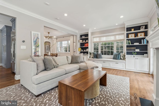 living area featuring light wood-style floors, ornamental molding, recessed lighting, built in features, and a chandelier