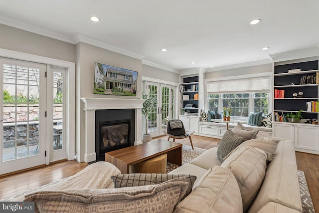 living room with recessed lighting, wood finished floors, crown molding, a glass covered fireplace, and french doors